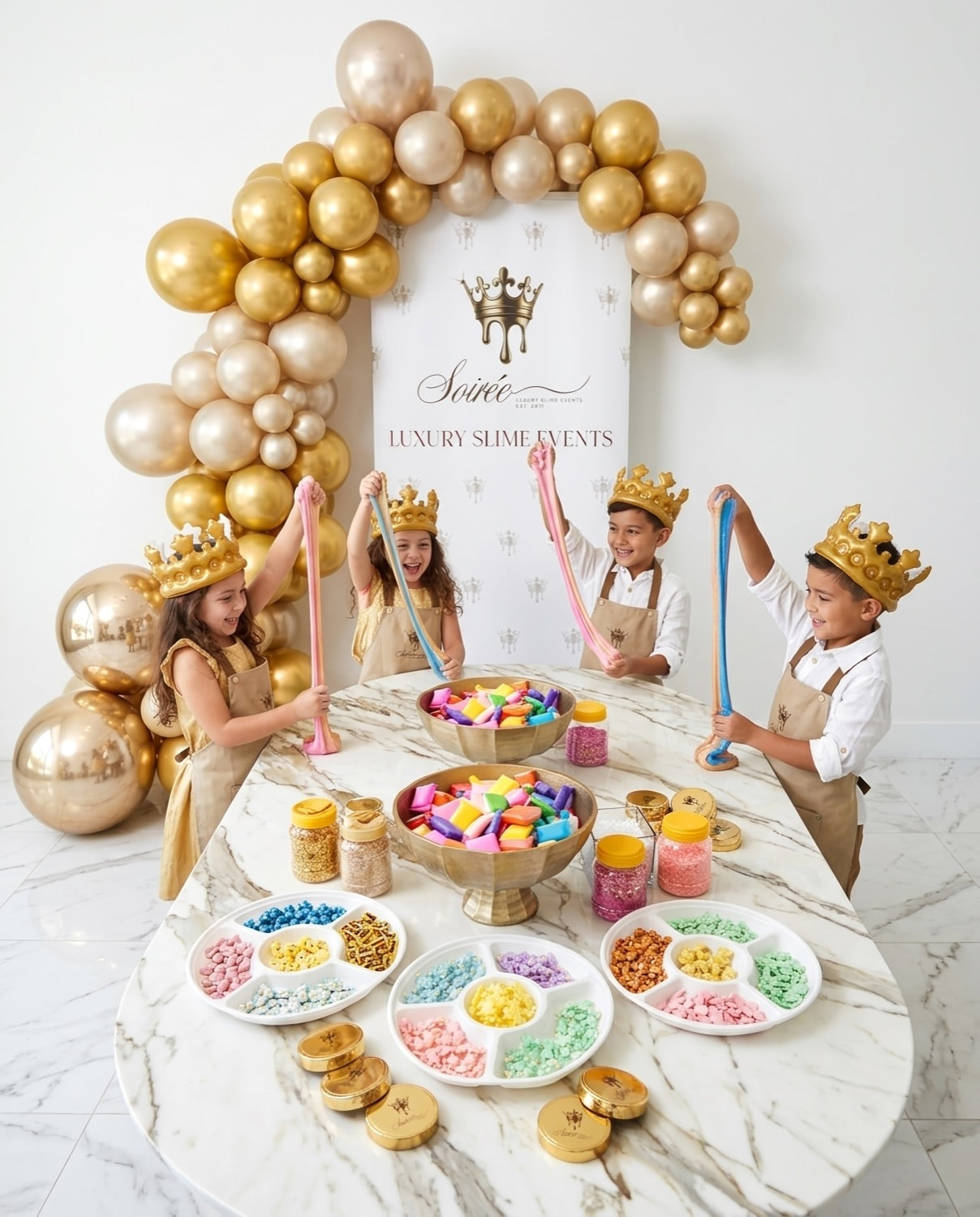 Children in gold crowns stretching slime around a white marble Slime Soirée table